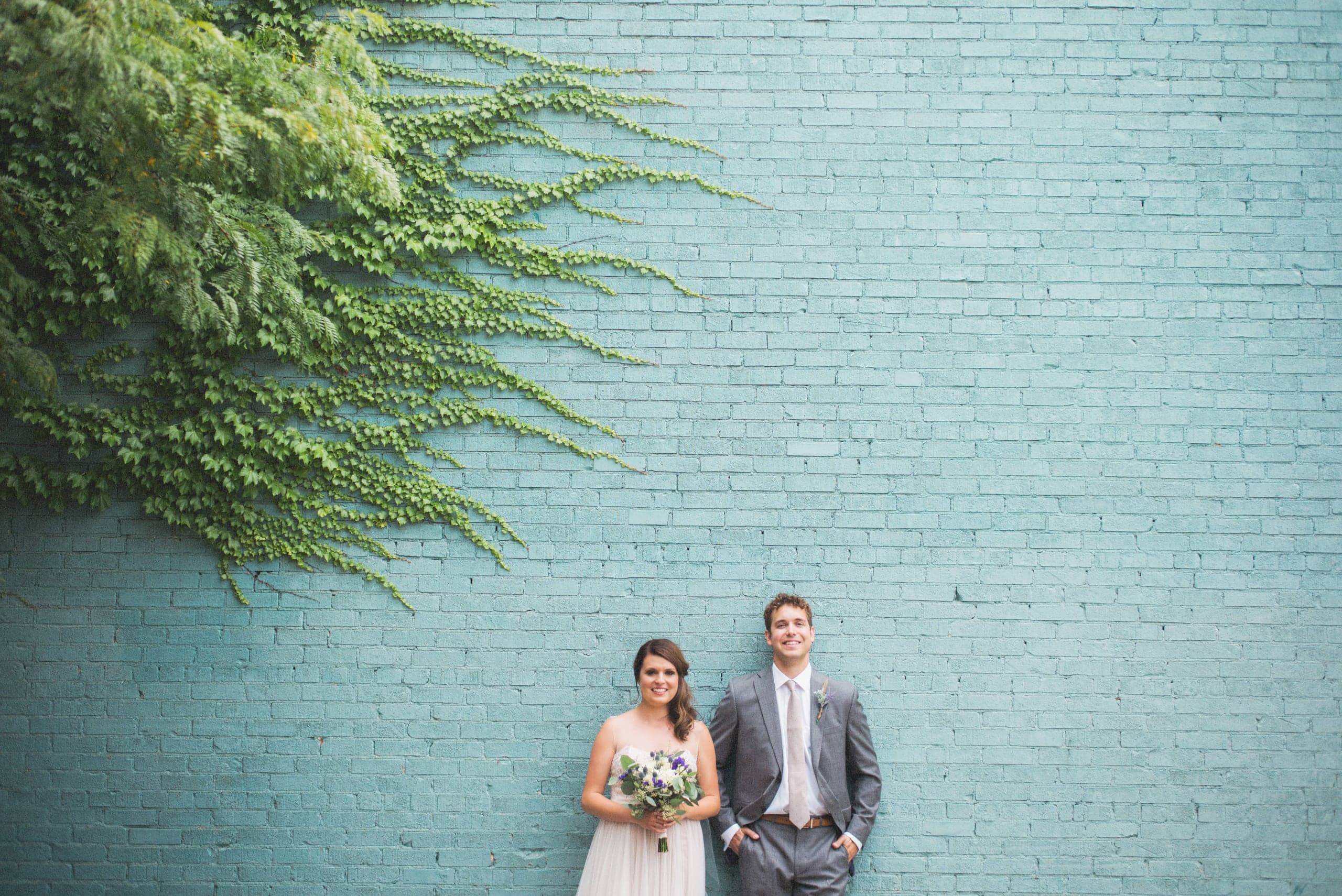 Bride and groom beneath an ivy-covered teal brick wall, by Iowa wedding photographer Studio Y